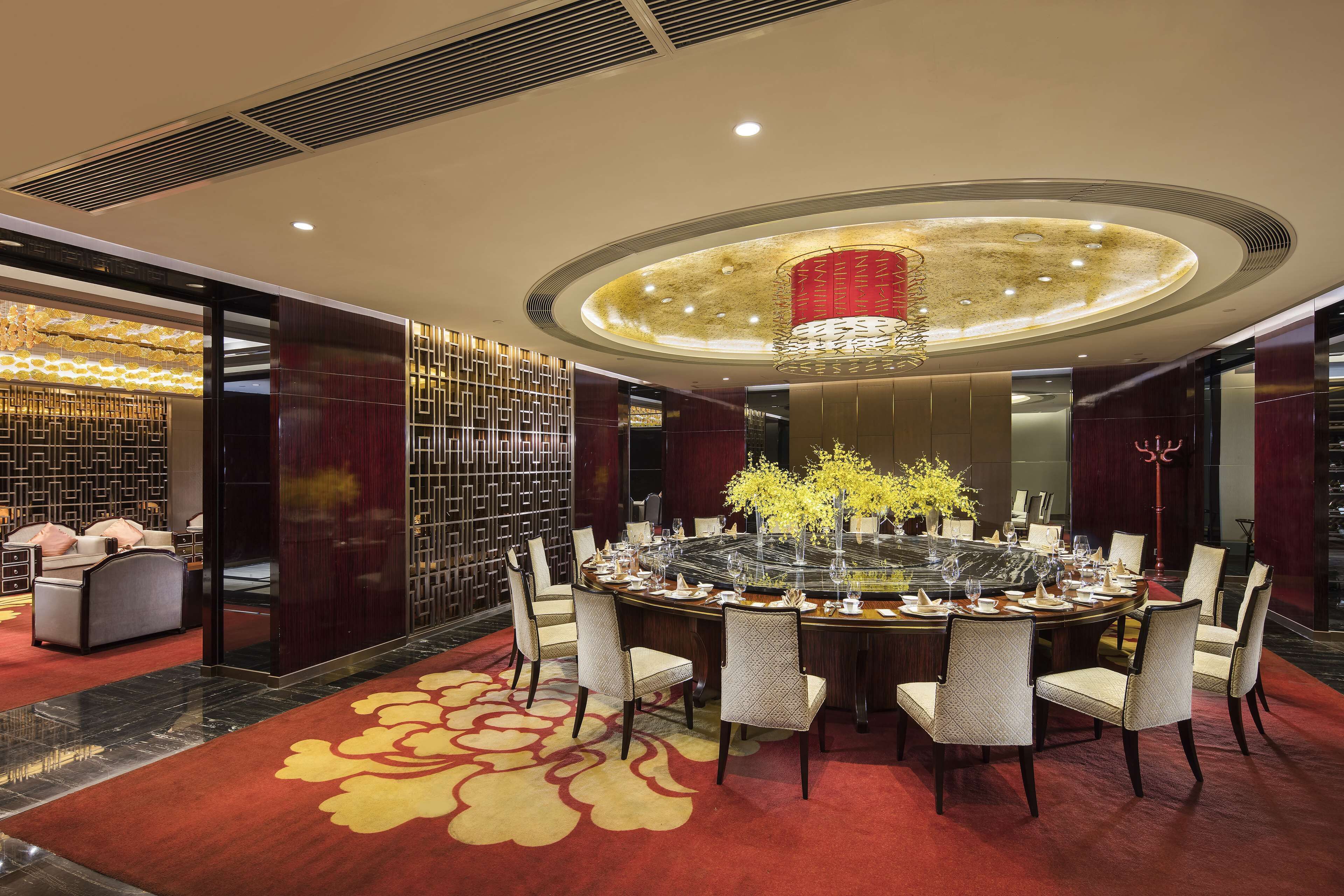 A round dining table with chairs, a chandelier, and a red carpet.