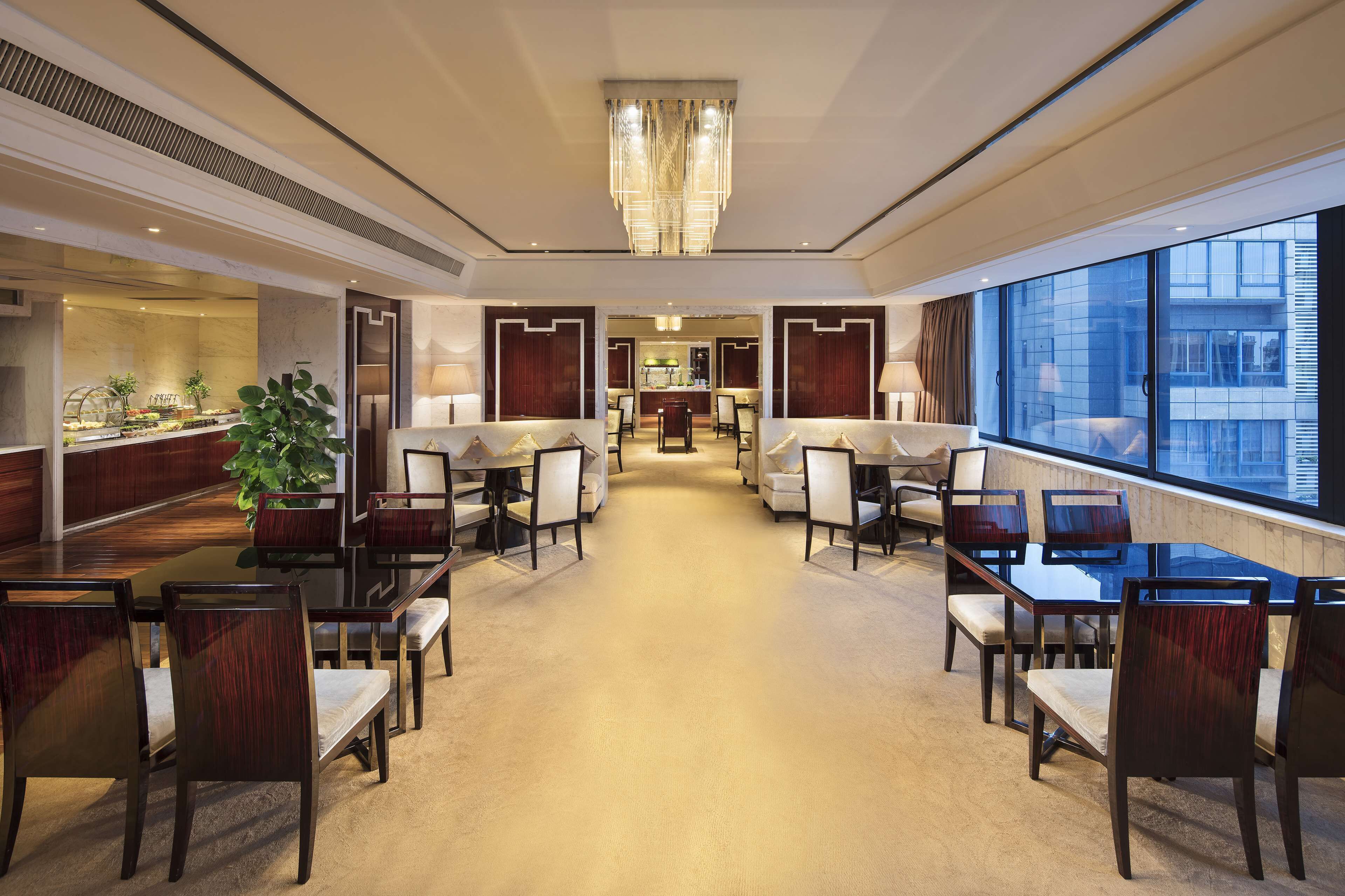 A spacious hotel lobby with a central seating area, a reception desk, and large windows offering a view of the city.