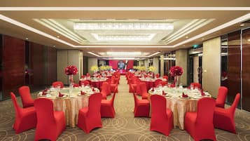 A banquet hall with multiple round tables, red chairs, and chandeliers.