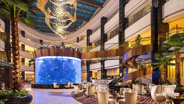 A spacious lobby with a central aquarium, multiple seating areas, and a grand staircase. - Hilton Foshan (Foshan)