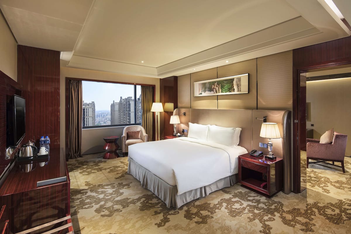 Habitación de hotel con una cama grande, un escritorio con una computadora, un televisor y una ventana con vista a la ciudad.