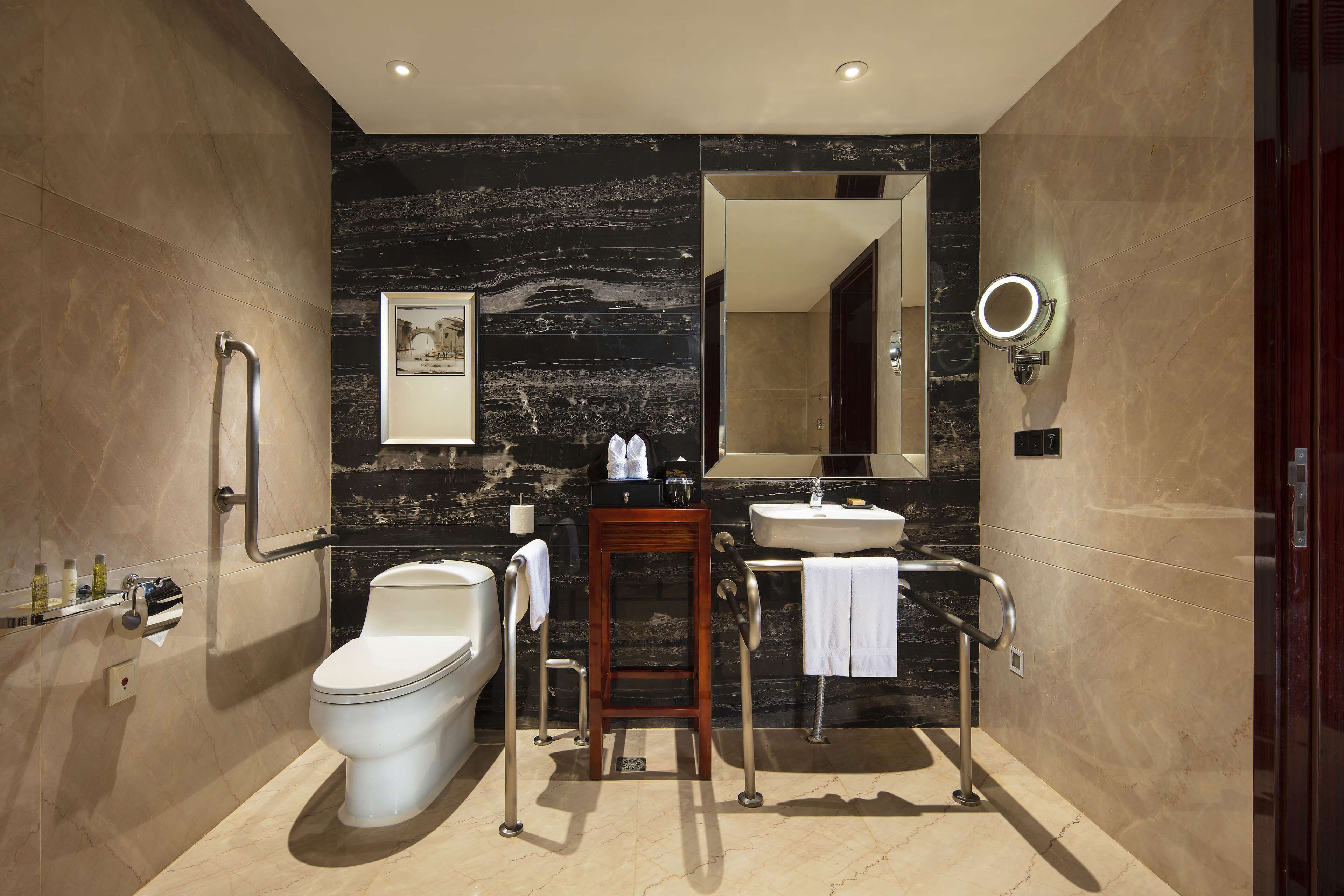 A modern bathroom with a toilet, sink, and vanity, featuring marble walls and a wooden stool.