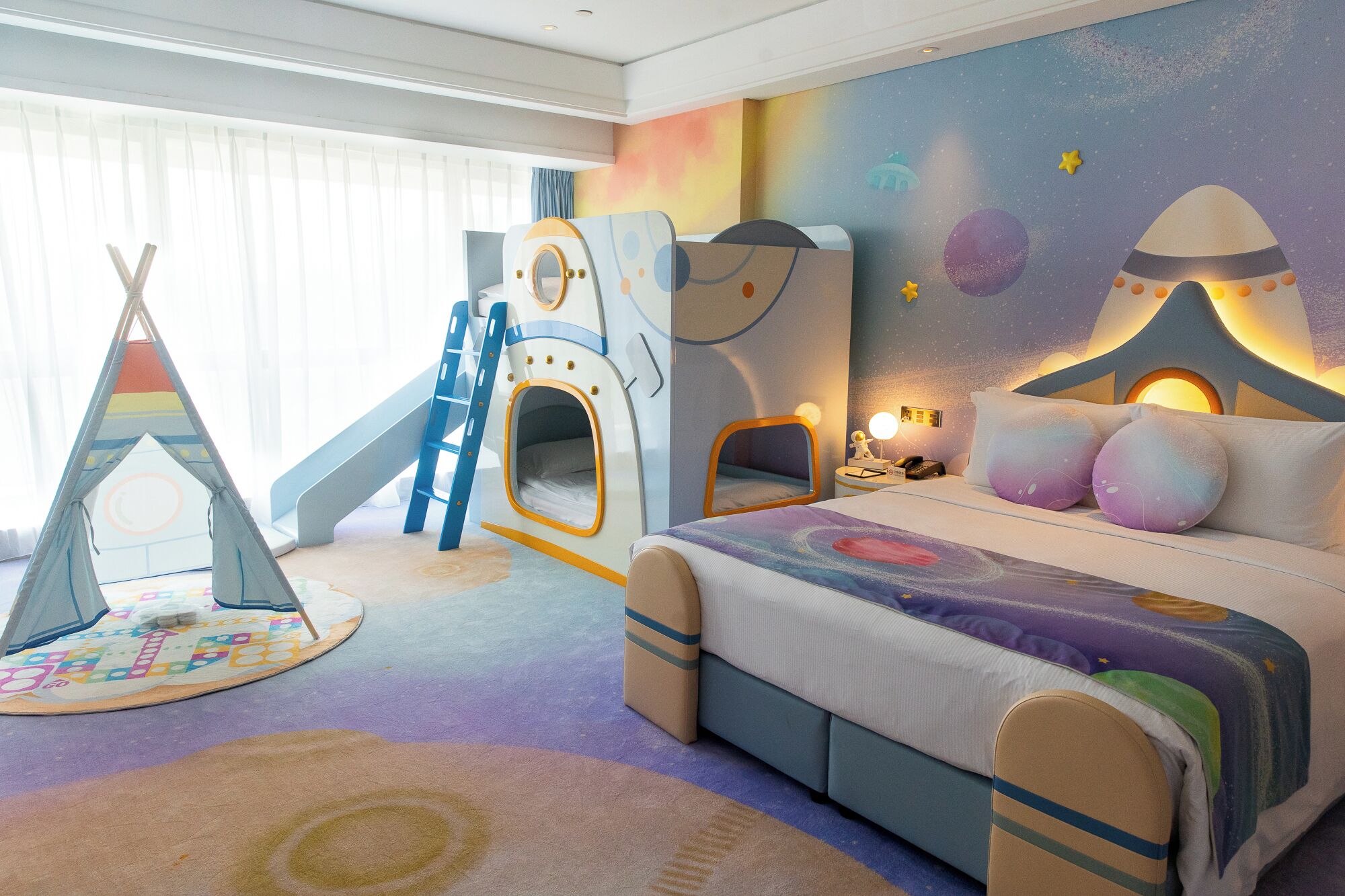 A child's playroom with a slide, a play tent, and a bed with a space-themed bedspread.