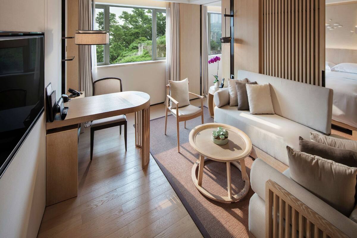 Quarto de hotel moderno com área de refeições, sofá, uma pequena mesa com uma planta e televisão.