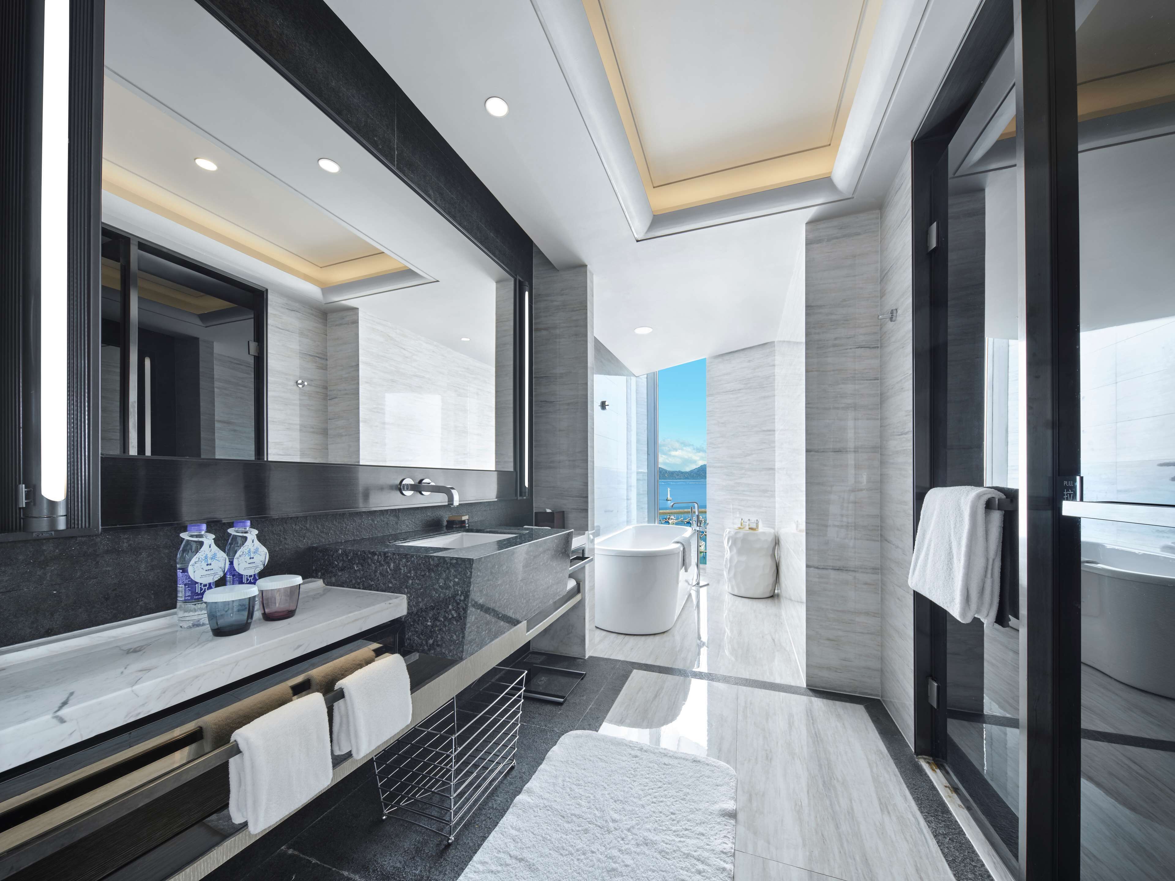A modern bathroom with a large mirror, a sink, a bathtub, and a shower. There are towels and toiletries on the counter.