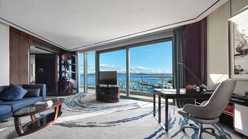 Ein modernes Wohnzimmer mit großem Fenster, einer Couch, einem Couchtisch, einem Fernseher und einem Schreibtisch mit Stuhl.