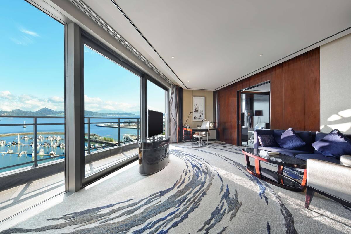 Quarto de hotel moderno com uma varanda grande, um sofá, uma mesa de centro e uma televisão.