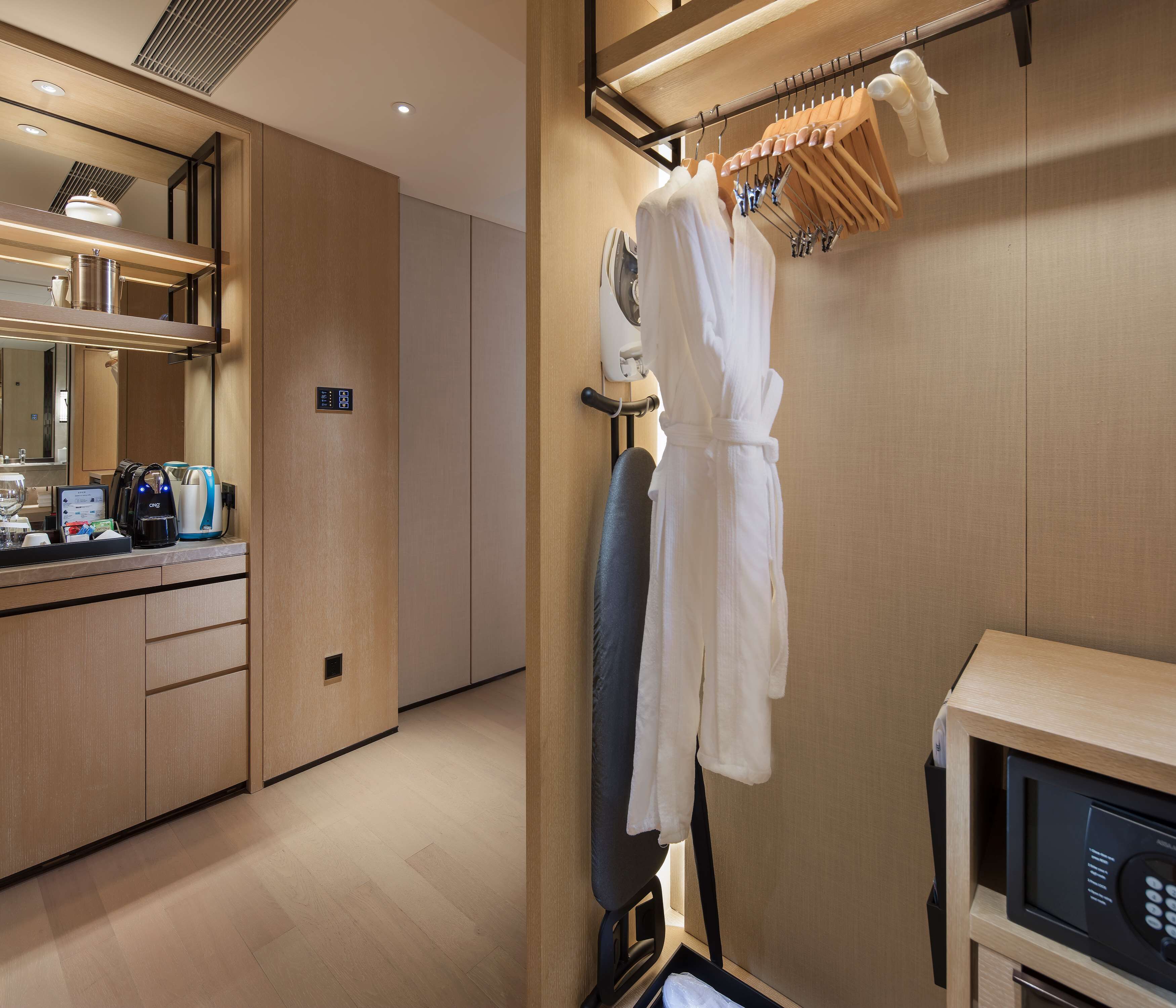 Habitación de hotel con tocador de madera, microondas, secador de pelo y bata colgada en un perchero.