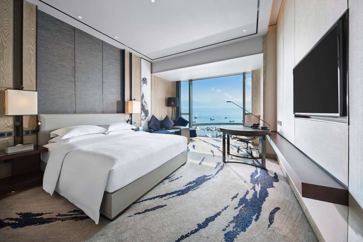 Quarto de hotel moderno com uma cama grande, uma escrivaninha e vista para o mar.