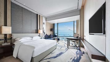 A modern hotel room with a large bed, a desk, and a view of the sea.
