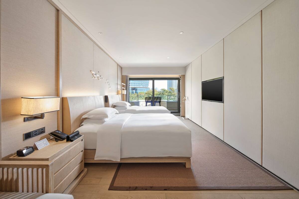 Quarto de hotel com uma cama grande, mesas de cabeceira, uma escrivaninha com telefone e televisão na parede.