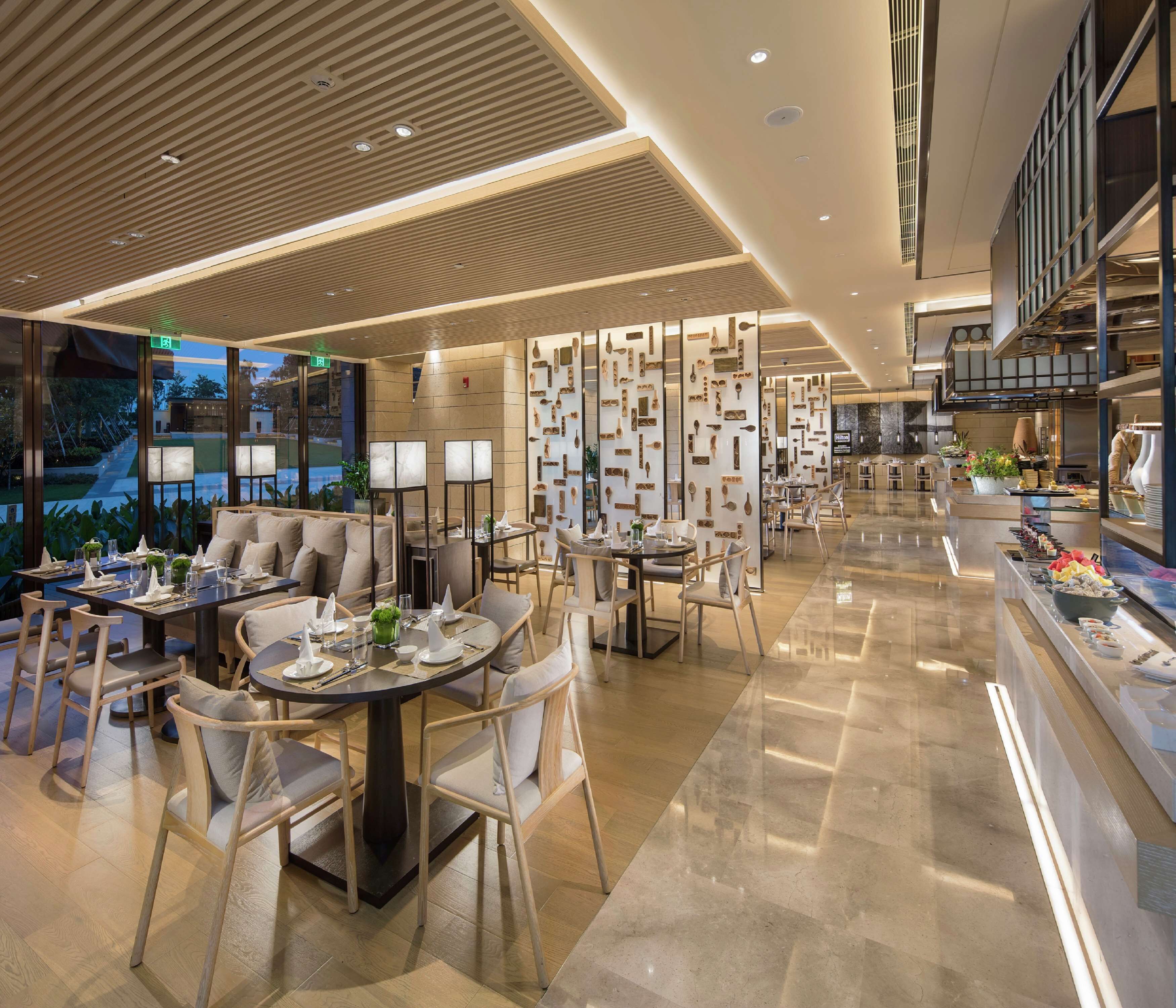 A modern hotel lobby with multiple seating areas, a central bar, and a view of the outdoors.
