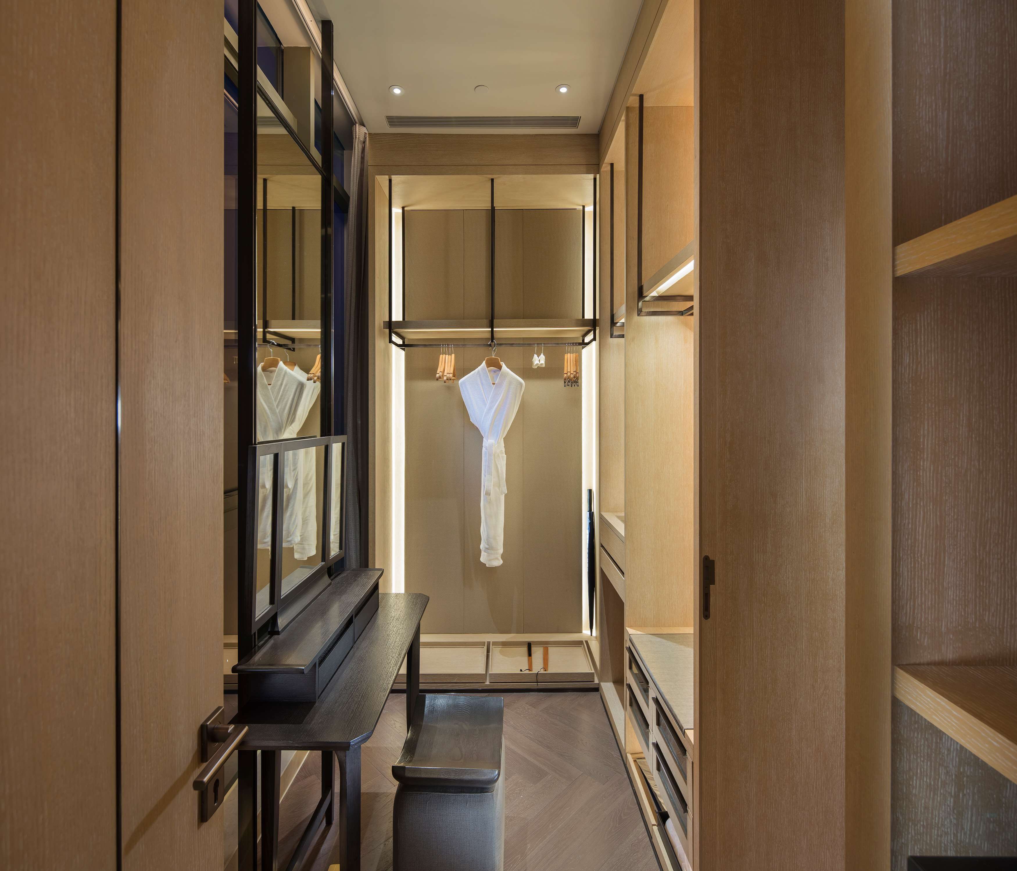 A modern bathroom with wooden cabinetry, a bench, and a robe hanging on a rack.
