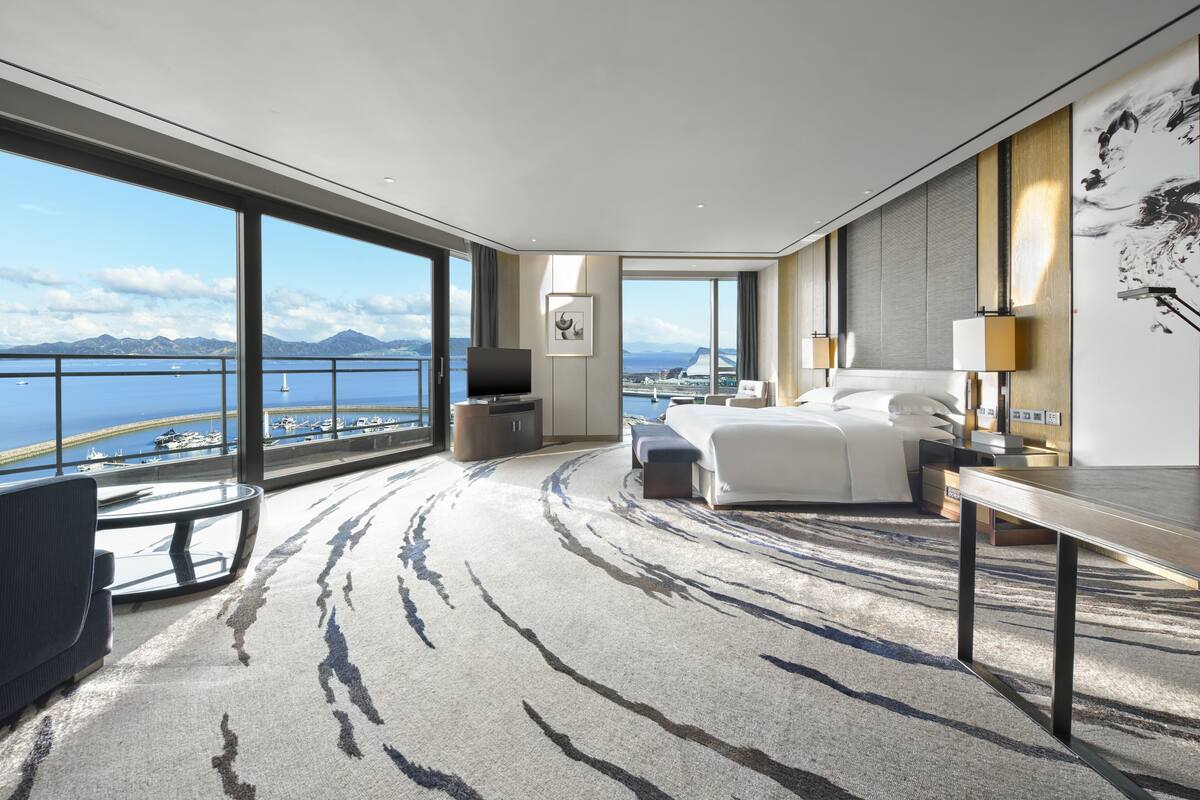Quarto de hotel moderno com uma varanda grande, uma cama, uma escrivaninha e uma televisão.