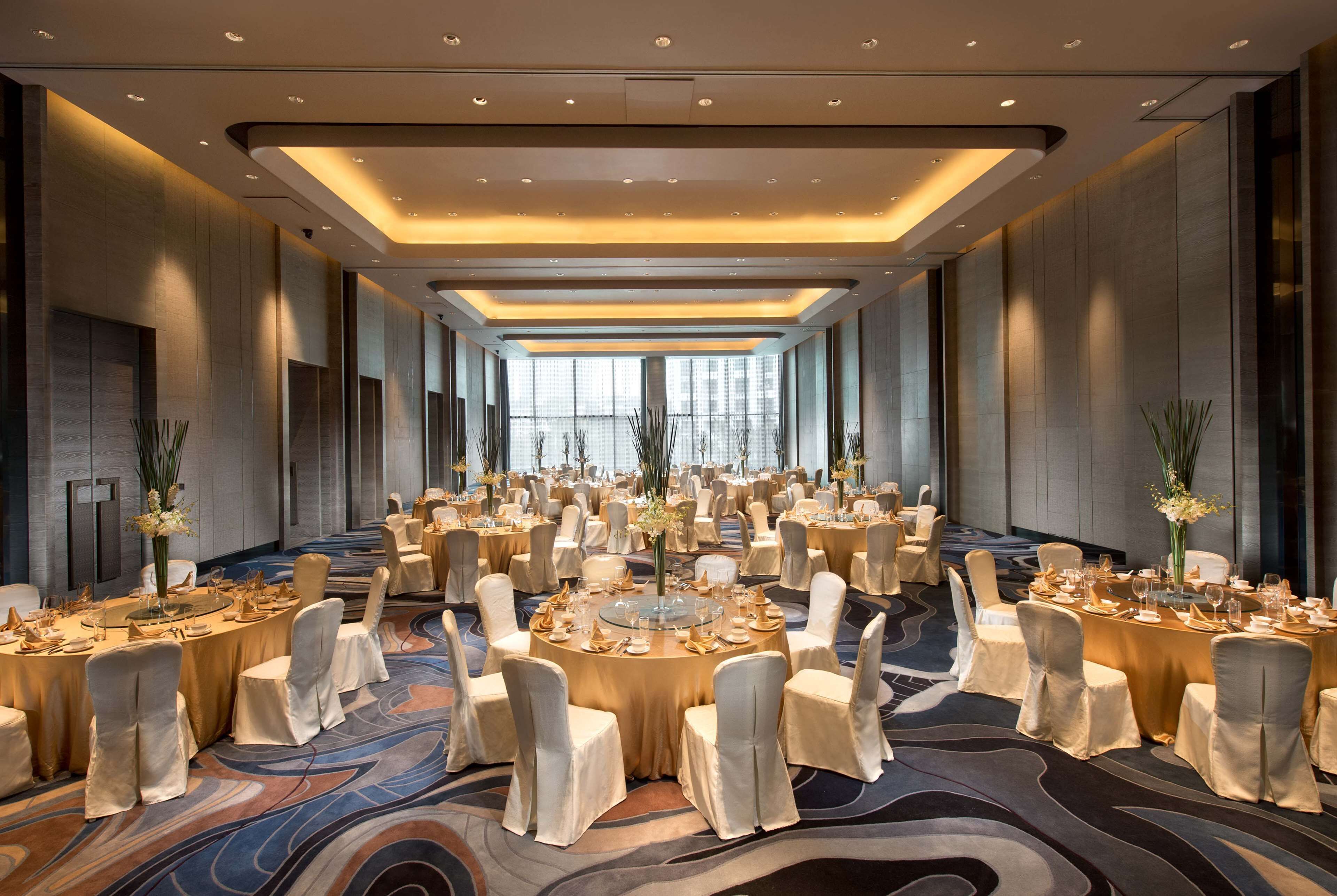 Une vaste salle de banquet avec des tables rondes, des chaises blanches et un sol recouvert de moquette.