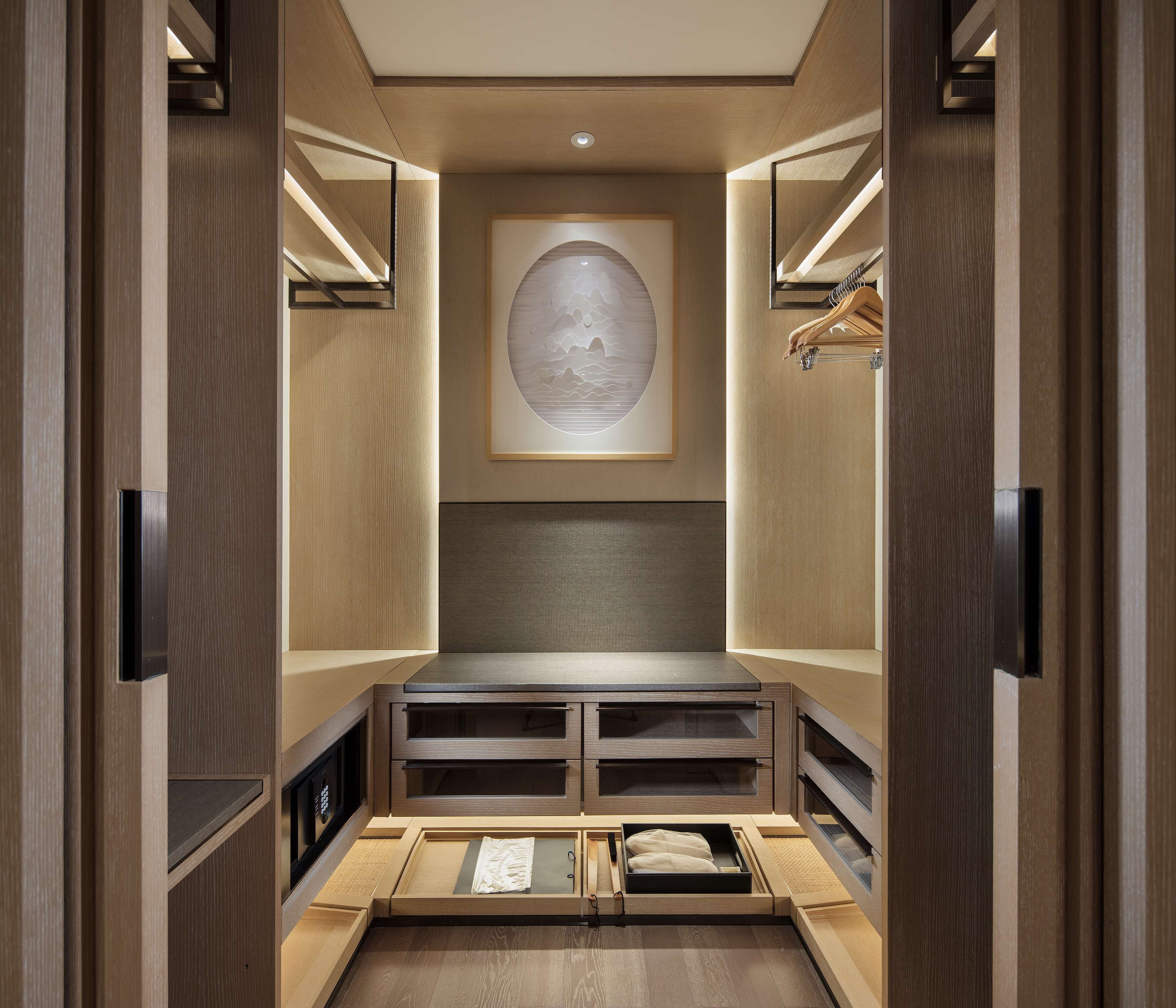 A walk-in closet with wooden doors, a recessed bench, and a framed artwork on the back wall.