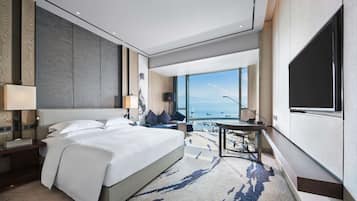 A modern hotel room with a large bed, a desk, and a view of the sea.