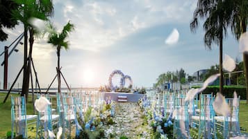 Eine Hochzeitslocation im Freien mit einem Blumengestall, Sitzgelegenheiten und Palmen.