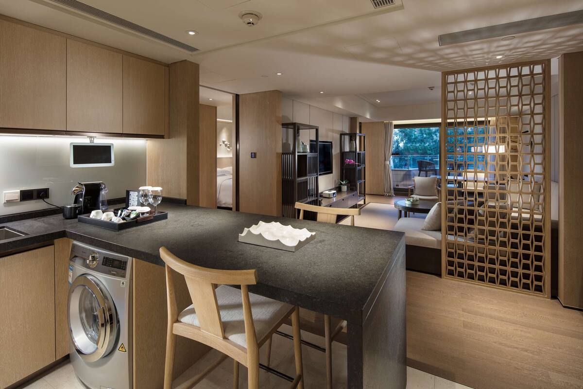 Cozinha moderna com máquina de lavar embutida, ilha central com banquetas e vista para uma varanda com área de estar ao ar livre.