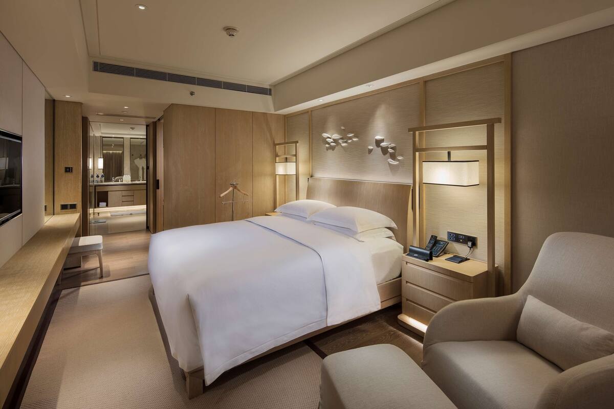 Quarto de hotel moderno com uma cama grande, mesas de cabeceira, uma escrivaninha e uma cadeira.