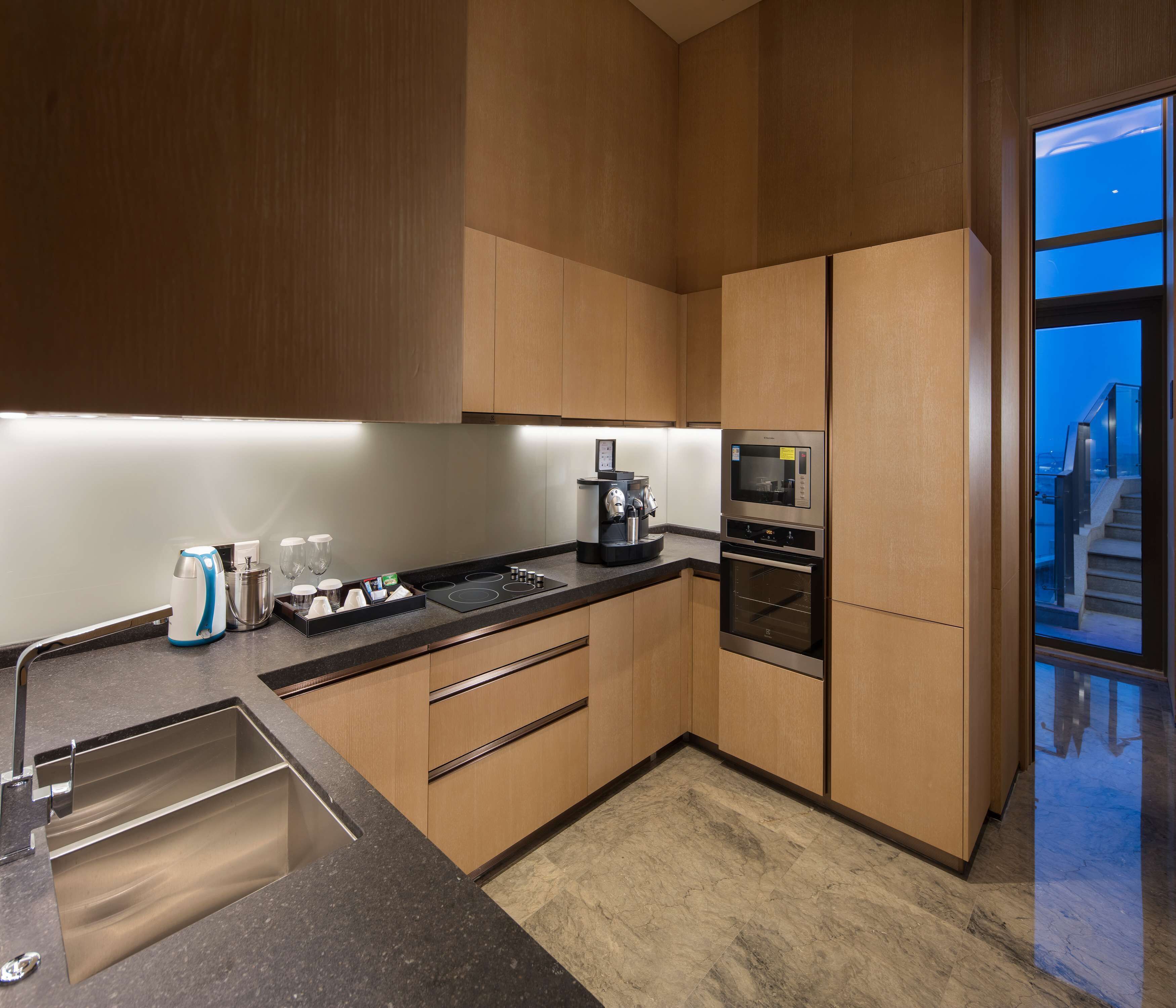 A modern kitchen with built-in appliances, a stainless steel sink, and a view of the city through a large window.