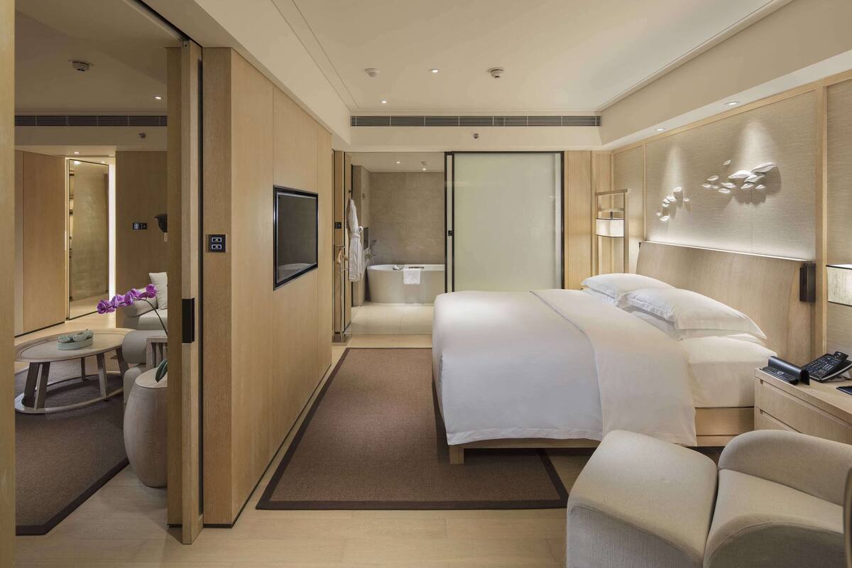 Quarto de hotel com cama, escrivaninha, cadeira, banheiro e televisão.