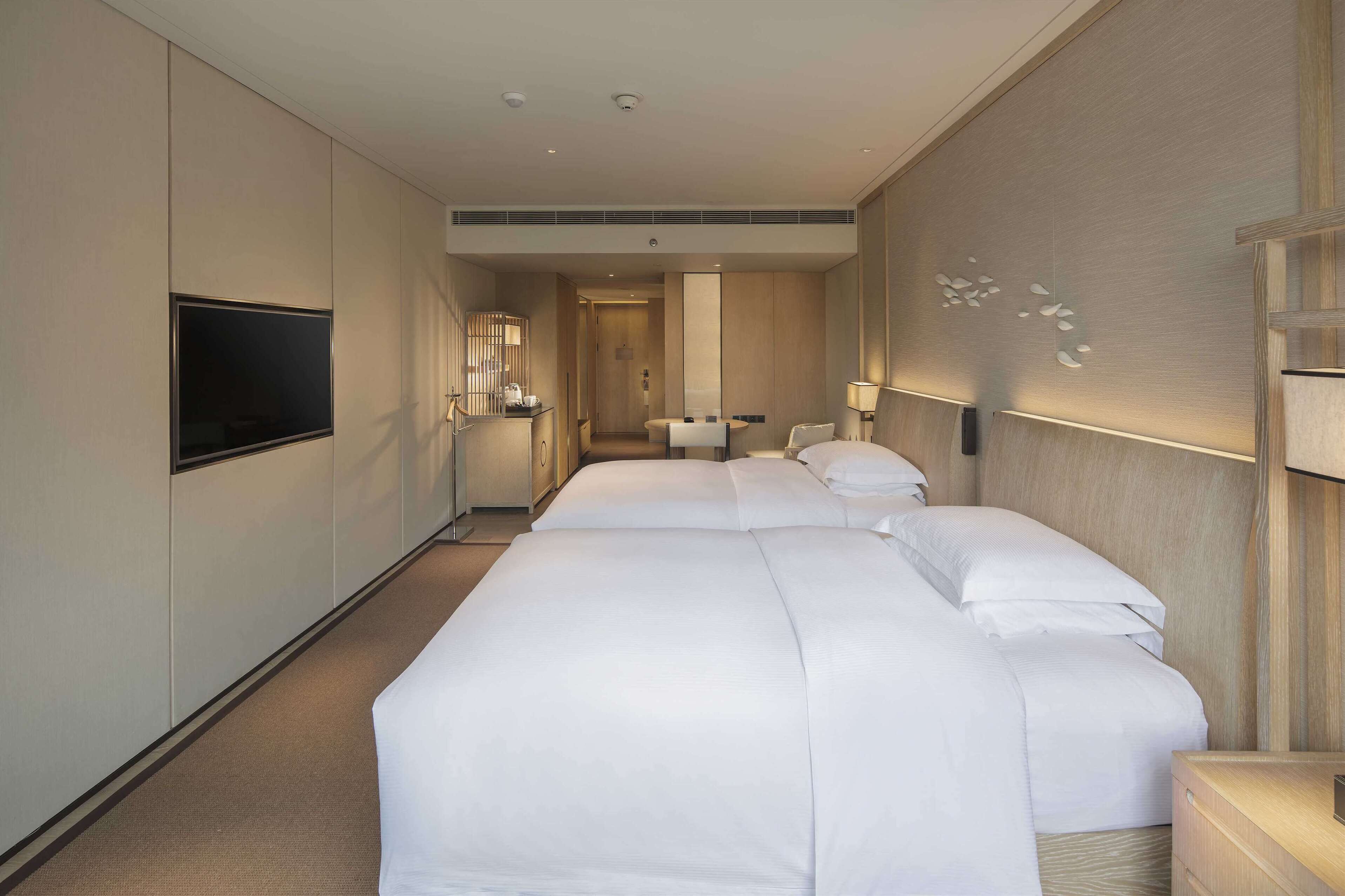Ein Hotelzimmer mit einem großen Bett, einem flachbildfernseher an der Wand, einem Nachttisch und einem Spiegel.