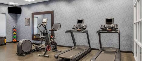 Un gimnasio con cintas de correr, elíptica y bicicleta estática.