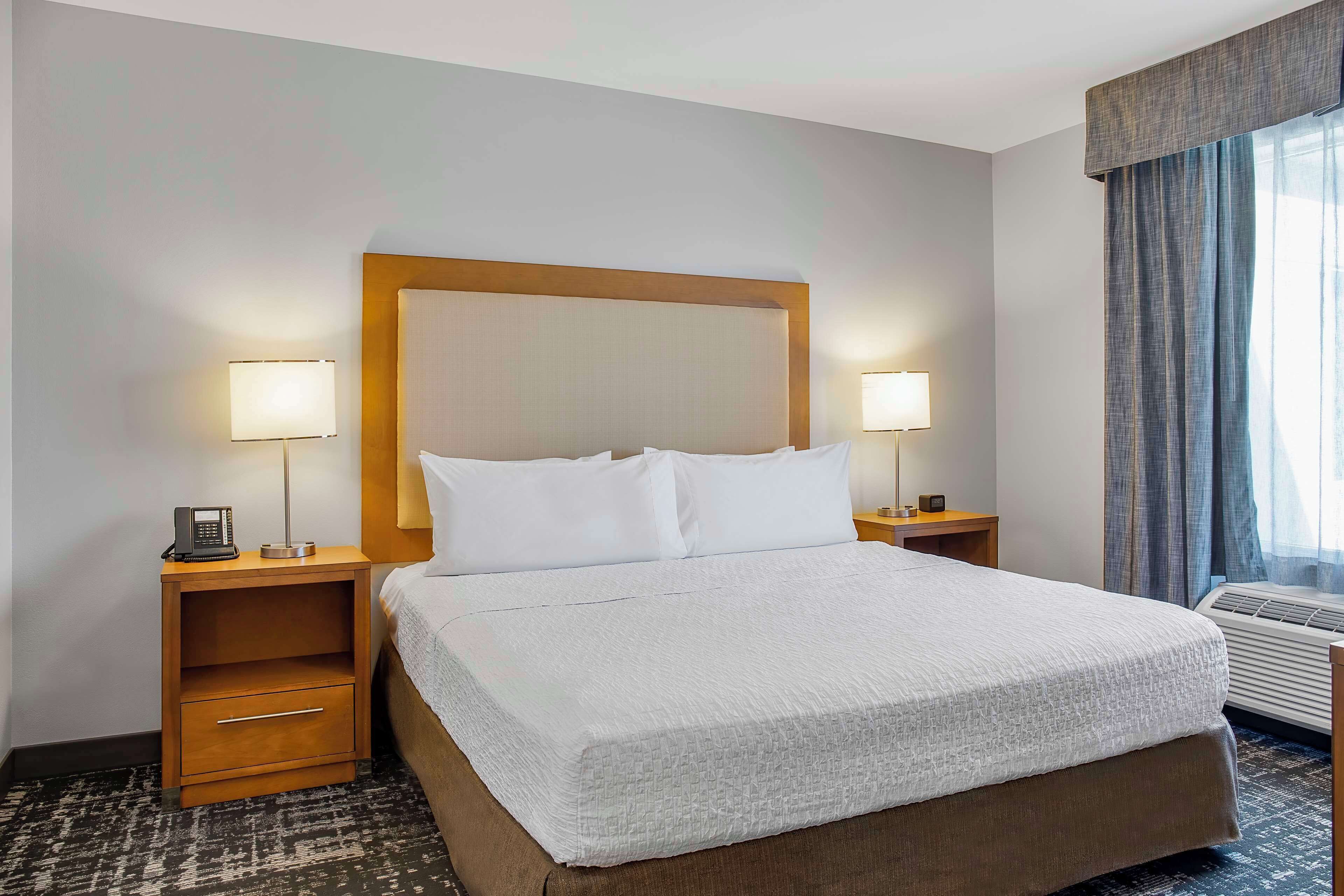 A hotel room with a large bed, two bedside tables with lamps, a bedside phone, and a window with curtains.