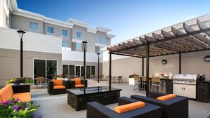 Ein möblierter Außenbereich mit Korbmöbeln, einem Grill und einer Pergola.