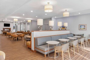 Un hall d’hôtel moderne, doté d’espaces aménagés avec des sièges, des tables et un écran de télévision.
