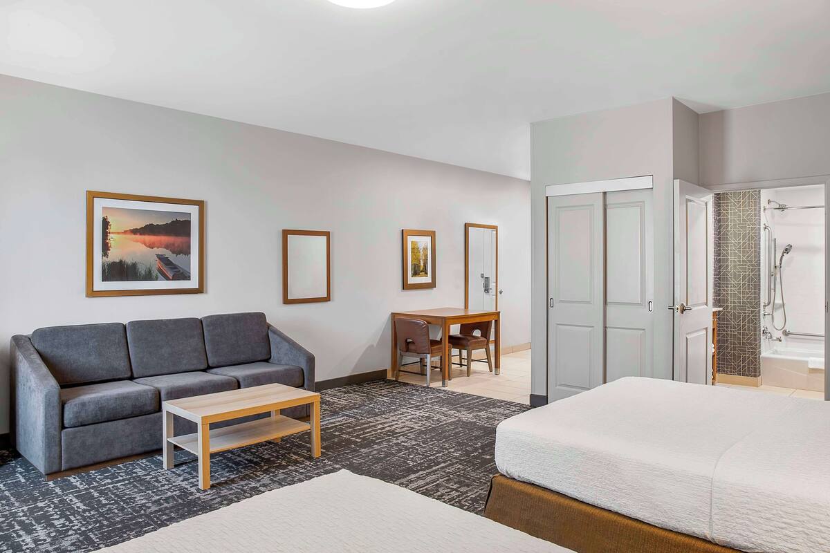 Ein Hotelzimmer mit grauem Sofa, einem Holztisch, einem Bett, einem Schreibtisch mit Stuhl und einem Badezimmer mit Dusche und Badewanne.