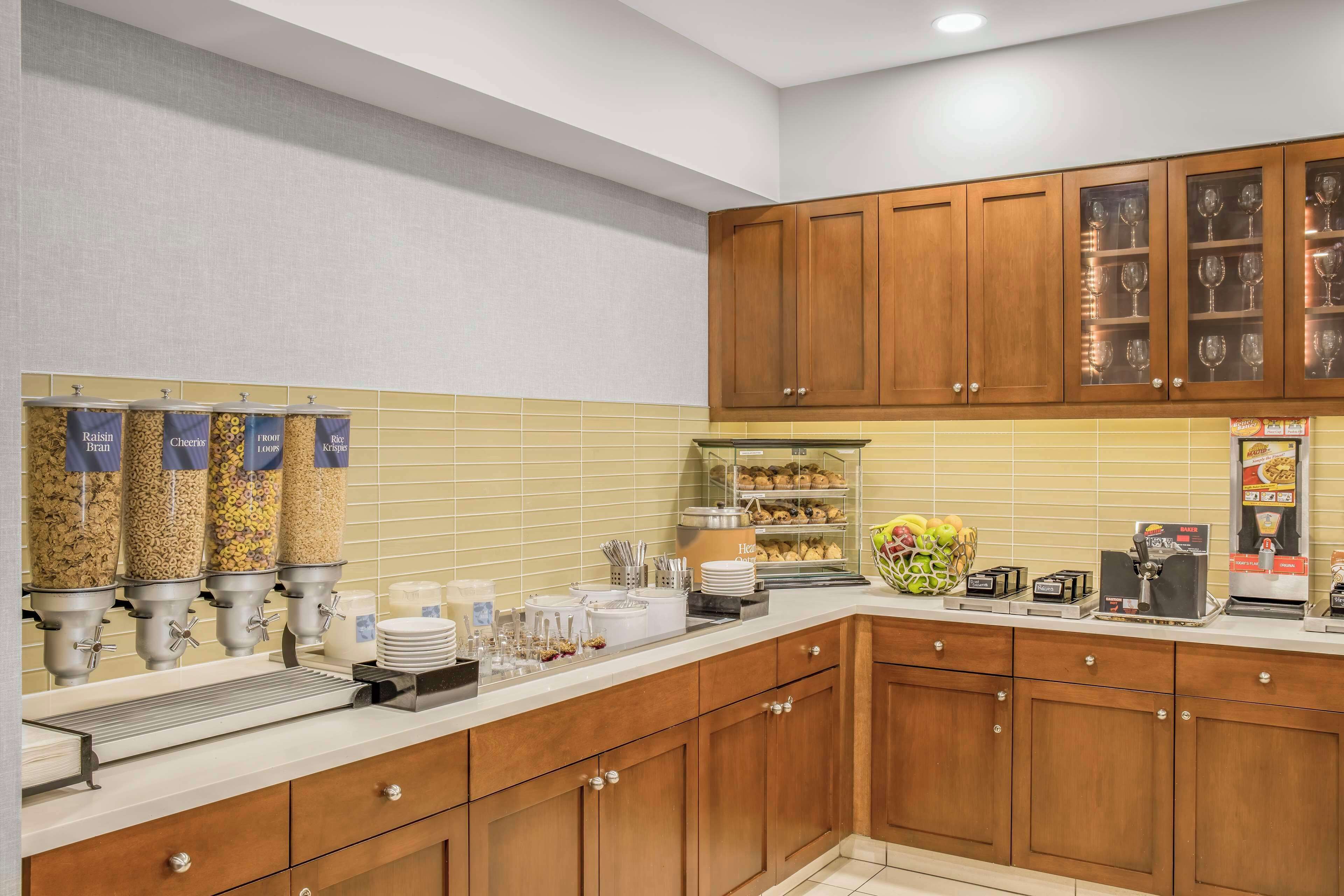 A kitchen with wooden cabinets, a buffet setup with food dispensers, and a coffee machine.