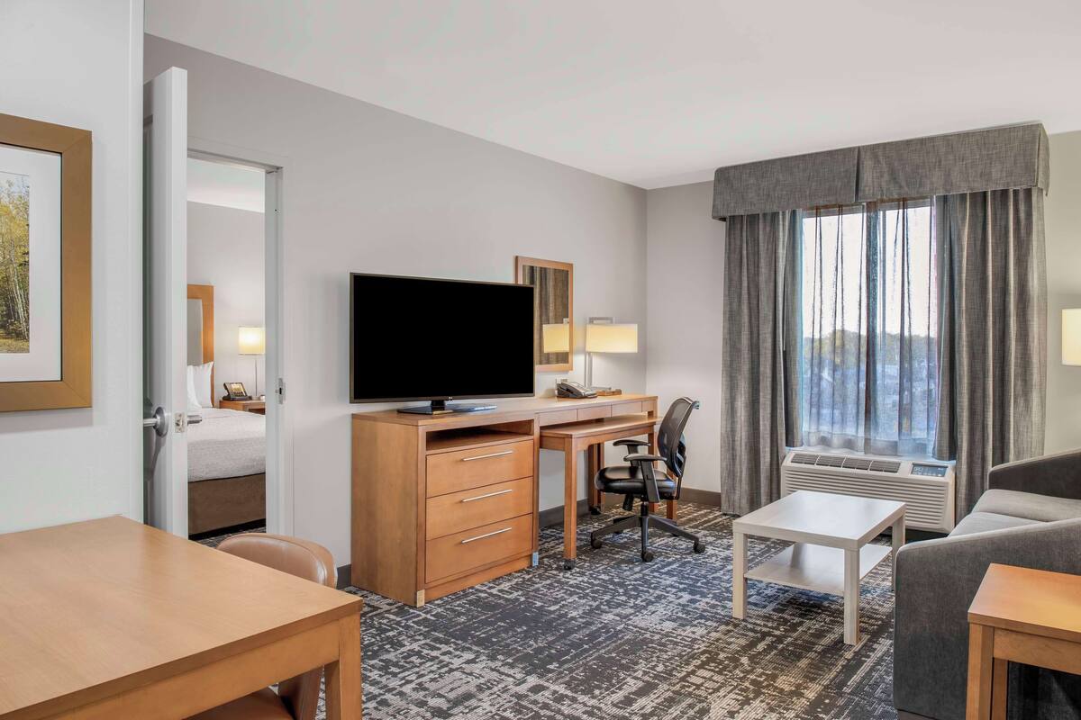 Ein Hotelzimmer mit Bett, Schreibtisch mit Computer, Fernseher, Sofa und einem Fenster mit Vorhängen.