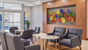 Eine moderne Lobby mit grauen Ledersesseln, einem hölzernen Empfangstresen und einer farbenfrohen Glasinstallation an der Wand.