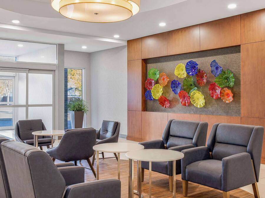 A modern lobby with grey leather chairs, a wooden reception desk, and a colorful glass art installation on the wall.