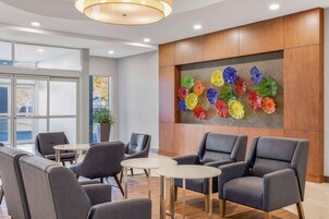Un lobby moderno con sillones de cuero gris, un mostrador de recepción de madera y una llamativa instalación artística de vidrio en la pared.