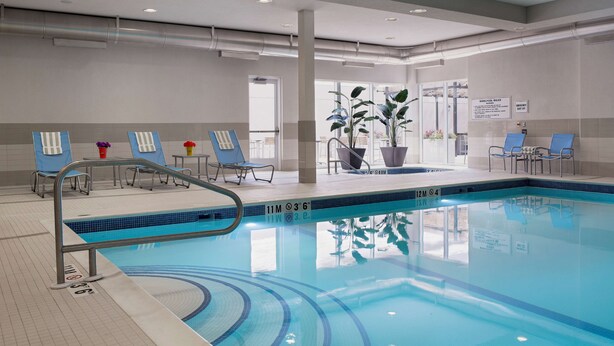 Ein beheiztes Hallenbad mit klarem Wasser, umgeben von Liegestühlen und Pflanzen in Töpfen.