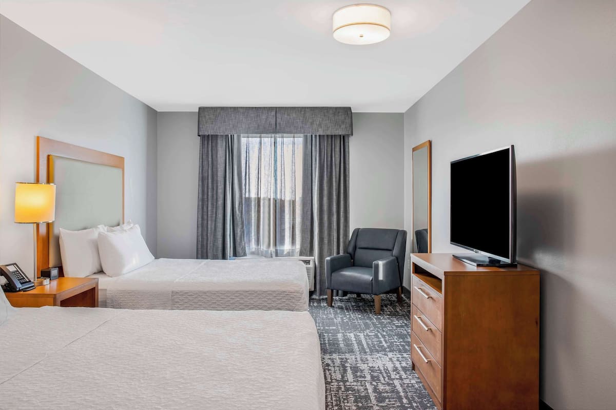 Ein Hotelzimmer mit zwei Betten, einem Fernseher, einem Sessel und einer Holzkommode.