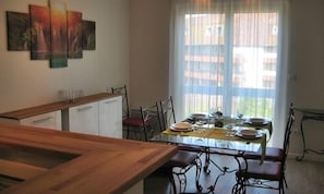 A dining area with a wooden table and chairs, a glass-top table, and a window with blinds. - Résidence le Beau Site (Capvern)