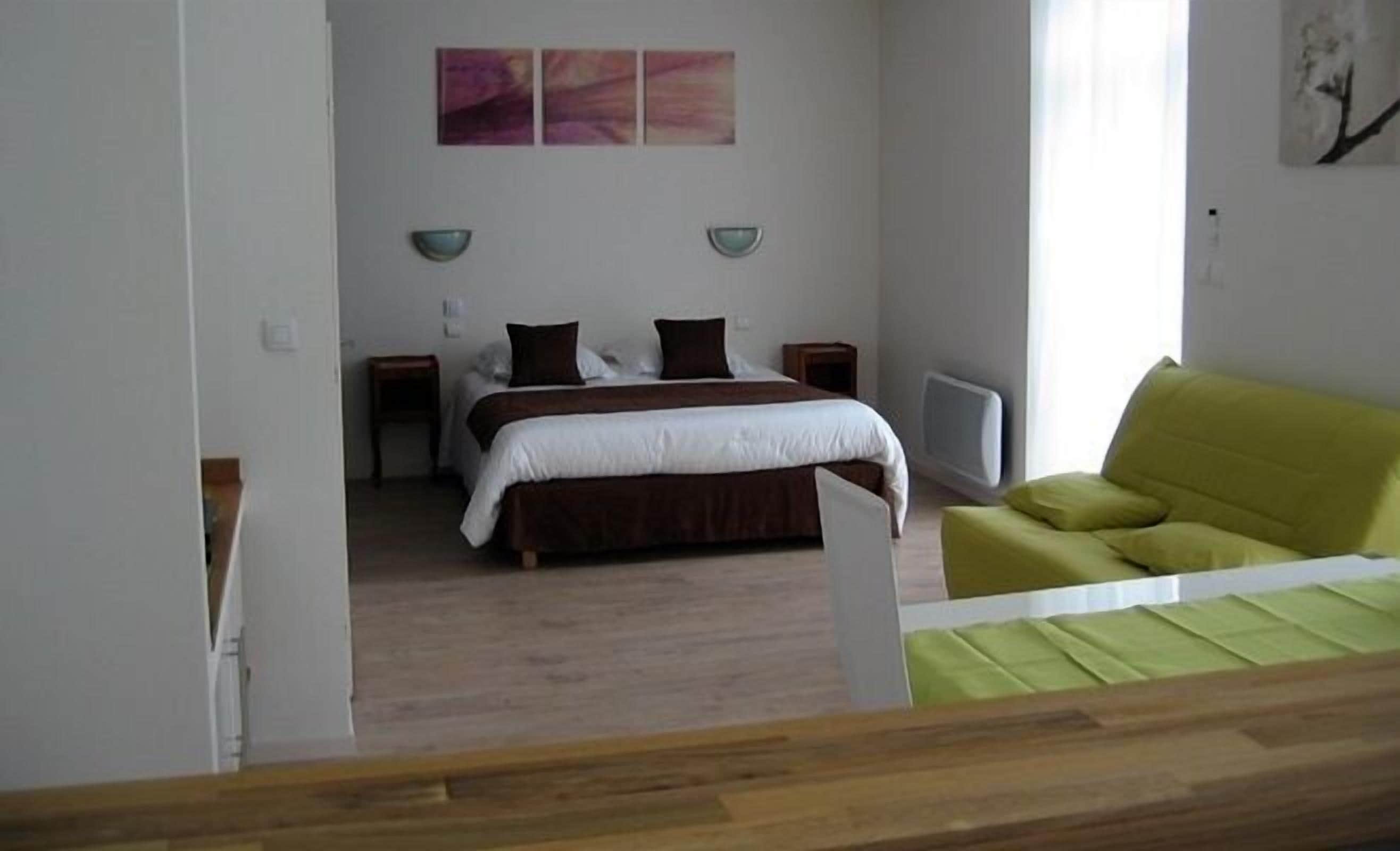 A bedroom with a bed, bedside tables, a green sofa, and abstract wall art.