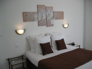 A neatly made bed with white and brown bedding, two wall-mounted light fixtures, and three wall art pieces above the bed. - Résidence le Beau Site (Capvern)