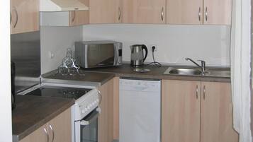 A compact kitchen with wooden cabinets, a microwave, a kettle, a dishwasher, and a stove.