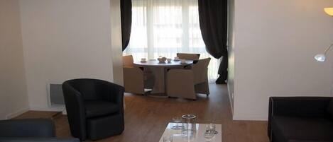 A living room with a coffee table, two armchairs, and a dining area with a table and chairs.