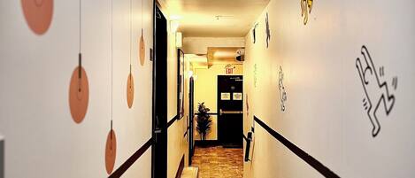 A hallway with a wooden floor, white walls, and black trim. There are circular wall decorations and a door with an exit sign.