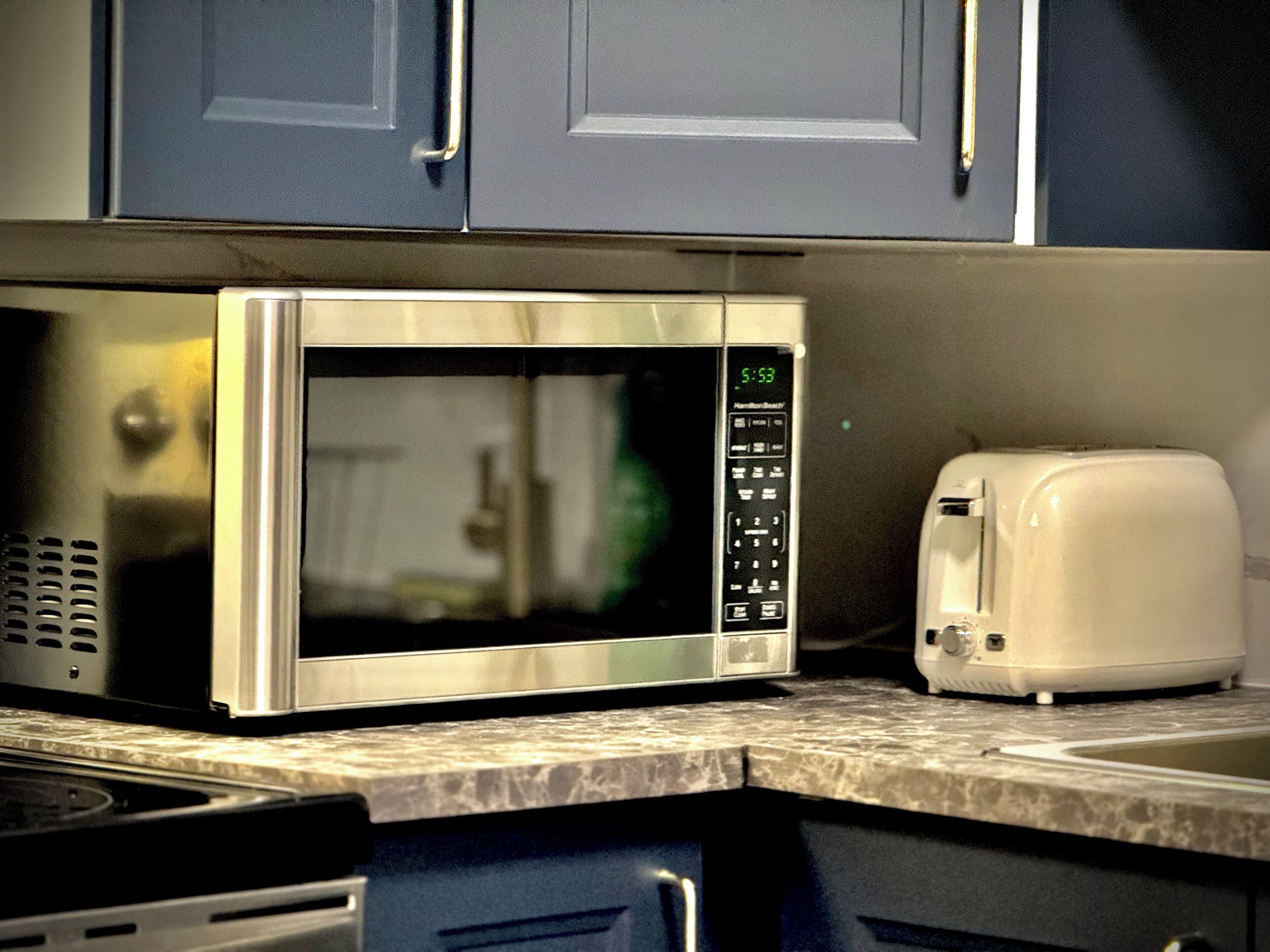 A kitchen with a stainless steel microwave, a toaster, and a marble countertop.
