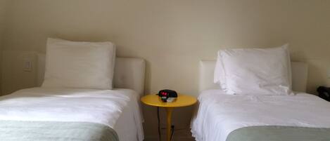 A hotel room with two single beds, a small round table with a clock, and a wall-mounted light fixture.
