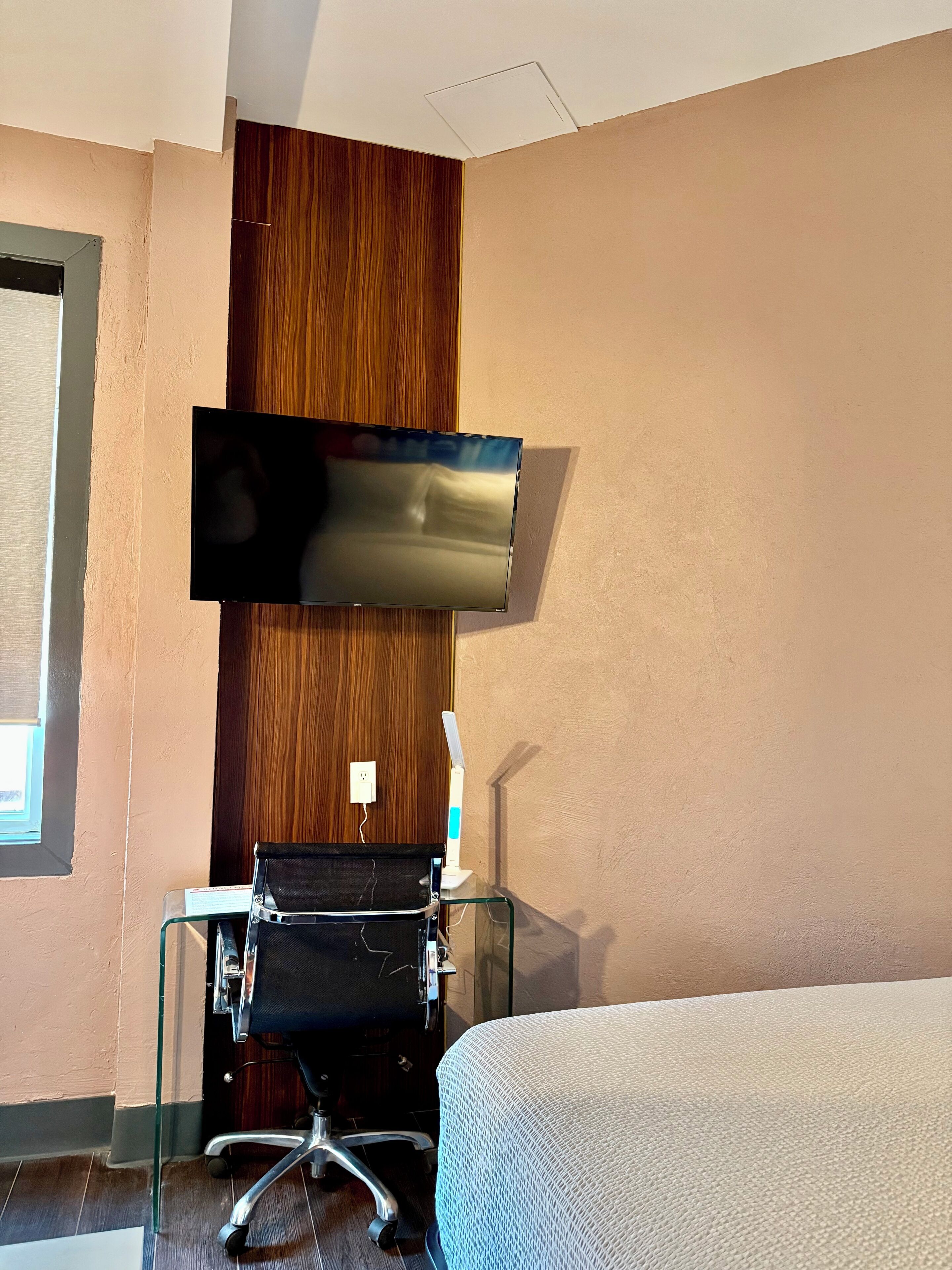 Habitación de hotel con cama, escritorio con silla, televisor de pantalla plana en la pared y ventana.