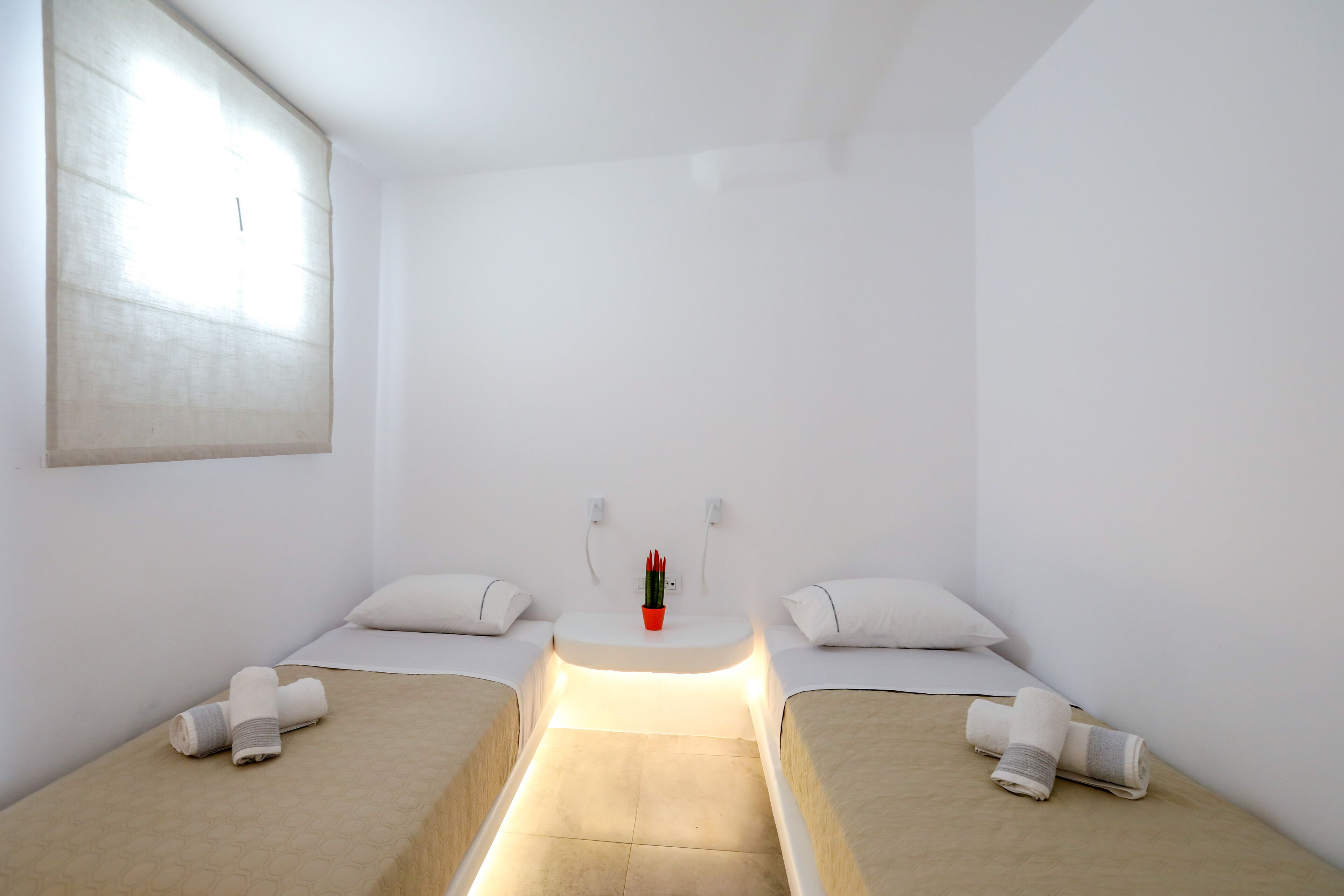 A minimalist hotel room with two single beds, a small bedside table, and a window.