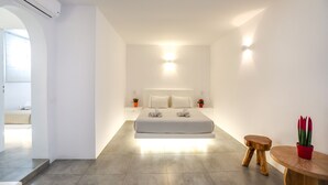 Quarto moderno com uma cama grande, mesas de cabeceira, uma mesa redonda de madeira e um vaso com planta.